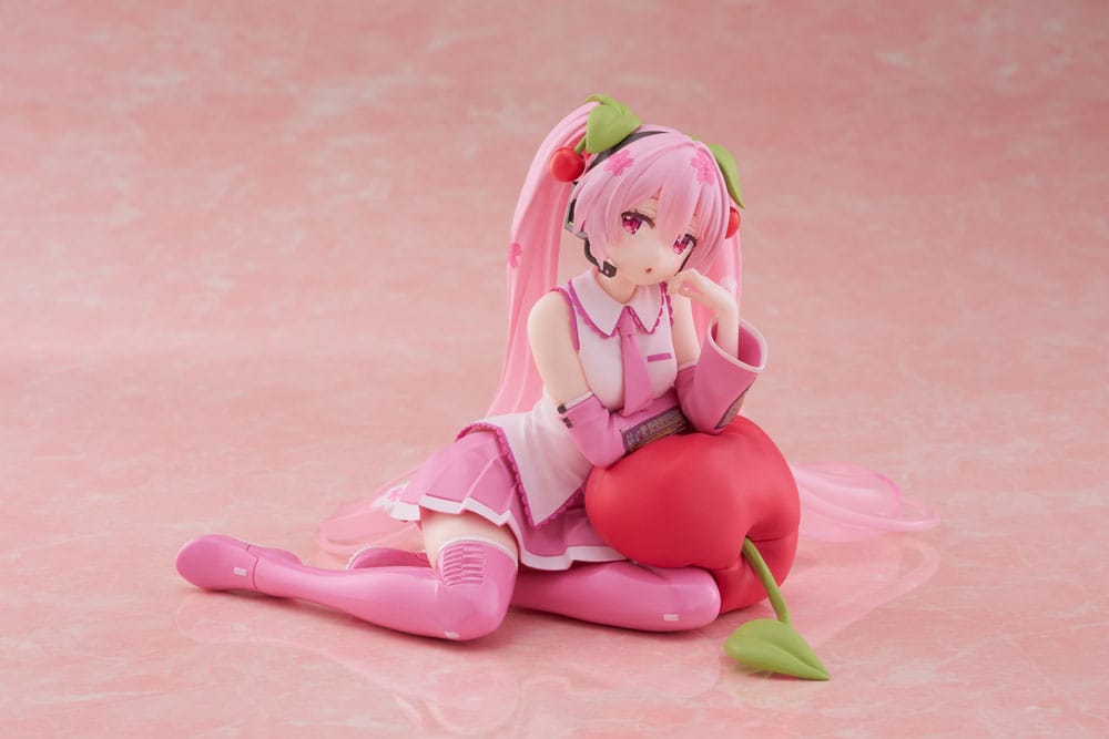Figurine Sakura Miku Cherry Cushion Ver. de 13 cm, assise contre un coussin cerise, cheveux roses décorés de fleurs et cerises, tenue rose détaillée et expression douce.