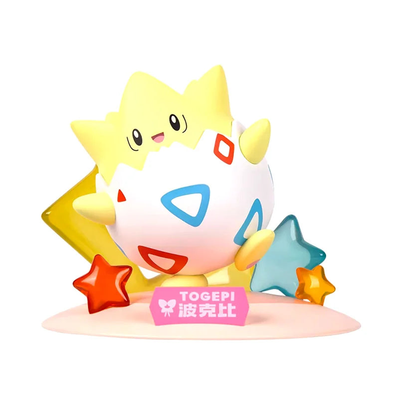 Figurine chibi de Togepi assis dans sa coquille décorée de motifs rouges et bleus, entouré d’étoiles colorées sur un socle rose. Une plaque rose avec son nom est posée à l’avant.