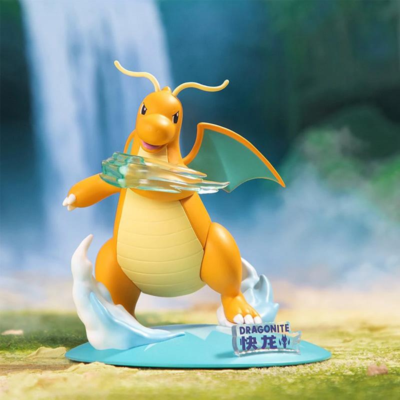 Figurine de Dracolosse (Dragonite) sur un socle bleu avec des effets de vagues et de vent. Il lance une attaque avec une projection translucide verte et jaune et arbore un grand sourire.
