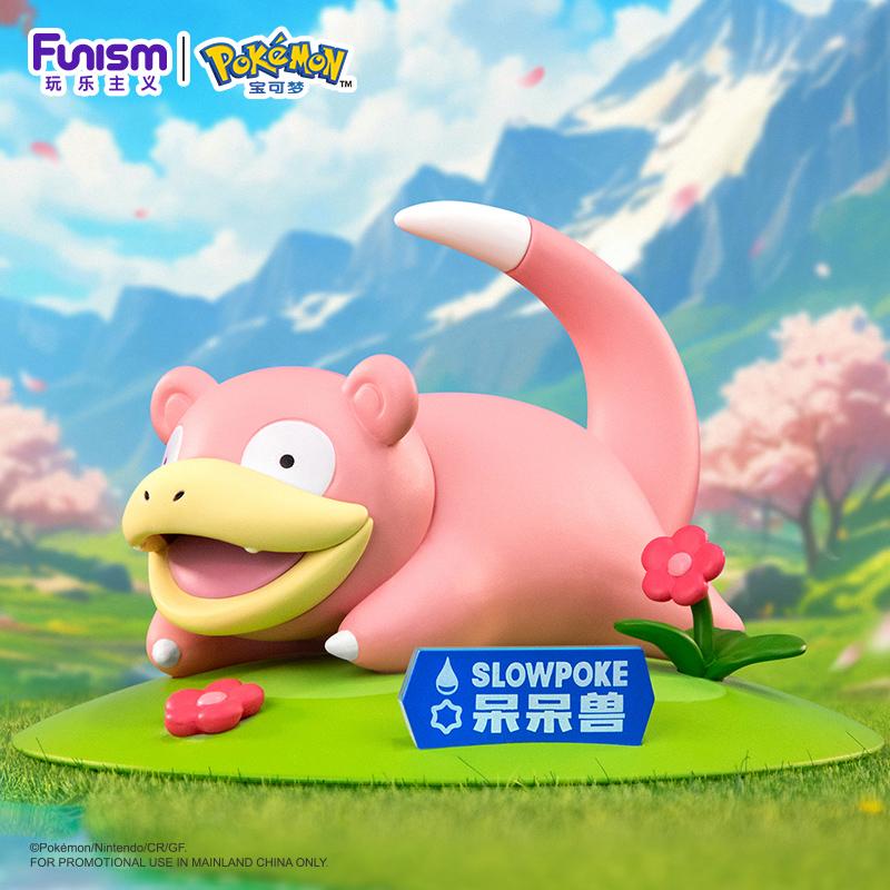 Figurine de Ramoloss (Slowpoke) allongé sur un socle vert avec des fleurs rouges. Le Pokémon a un grand sourire et une plaque bleue avec son nom figure devant lui. En arrière-plan : décor de montagnes et cerisiers en fleurs.