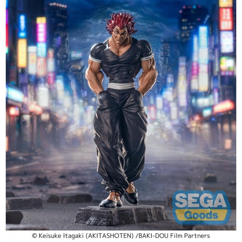 Figurine Baki Luminasta Yujiro Hanma par Sega, représentant Yujiro en tenue noire, mains dans les poches, cheveux rouges et posture menaçante sur un socle urbain.