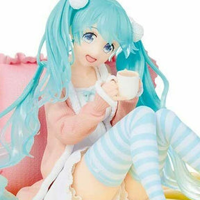 Figurine de Hatsune Miku en tenue pastel décontractée, assise avec une tasse dans les mains, ambiance cosy et kawaii.
